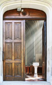 Front door of a church with light streaming inside